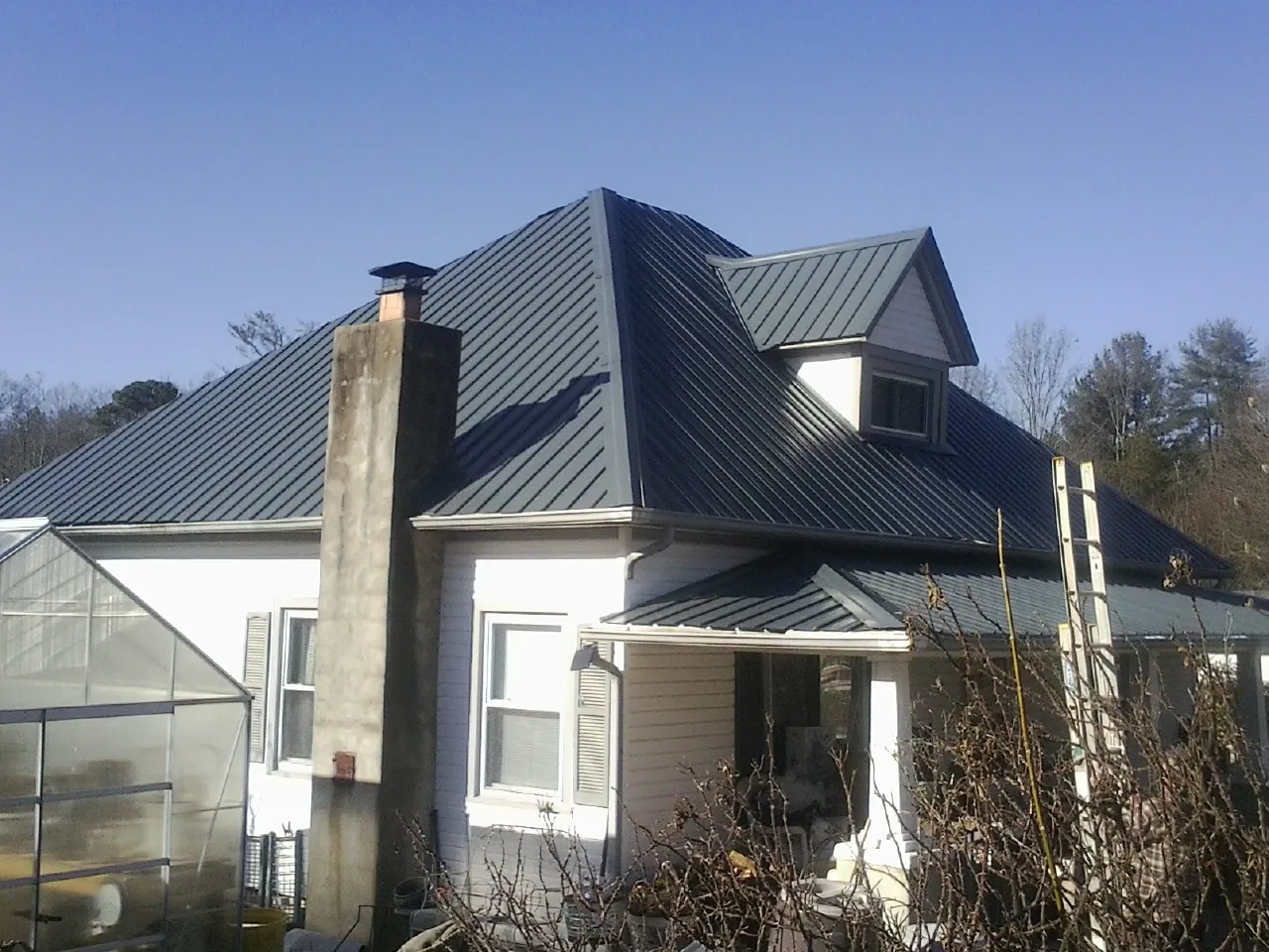 Dark blue standing seam metal roof on a white farmhouse with dormer — Slate & Tile Roof Repair by Roofing Brothers in Milano
