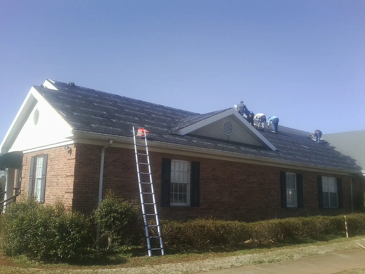 Crew tearing shingles off a brick ranch roof with a ladder set — Metal Roof Repair work by our crew in Milano