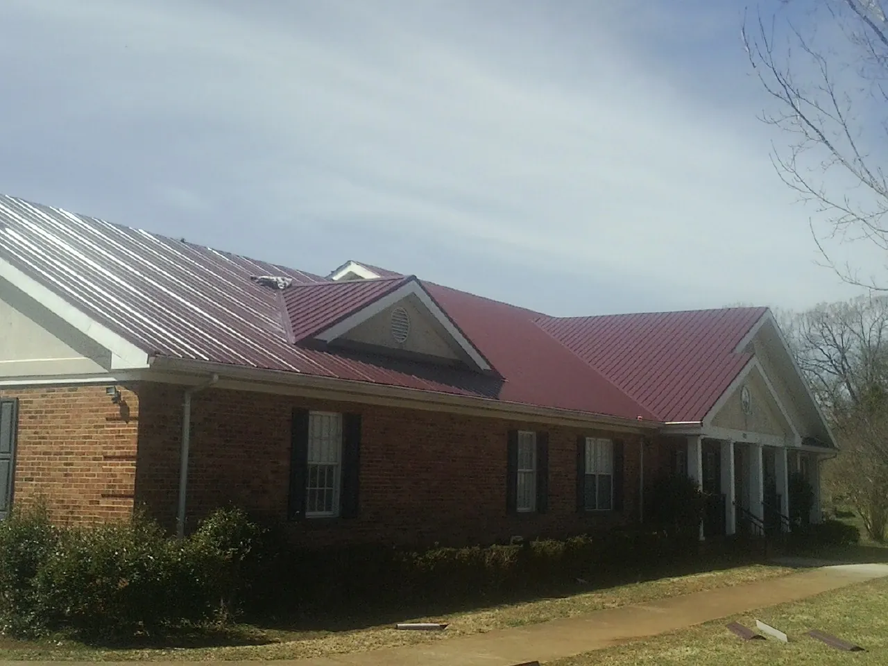 Red metal roof with gabled entries on a long brick building, from a Hail Damage Roof Repair job in Milano