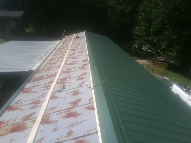 Old rusted panels beside newly installed green metal roofing — Wind Damage Roof Repair by Roofing Brothers in Milano