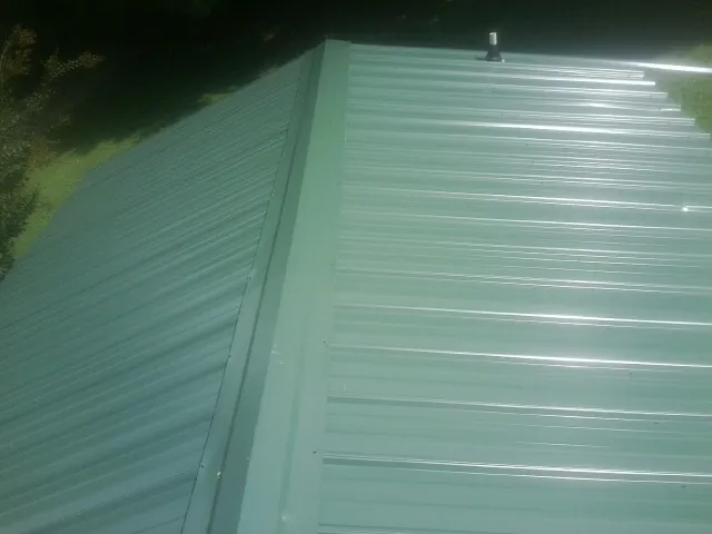 New green metal panels meeting at the ridge of a roof — Flat Roof Repair work by our crew in Milano