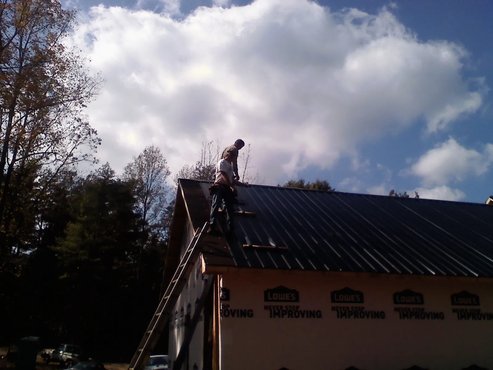 Roofer fastening dark metal panels high against a cloudy sky, from a Roof Inspection job in Milano