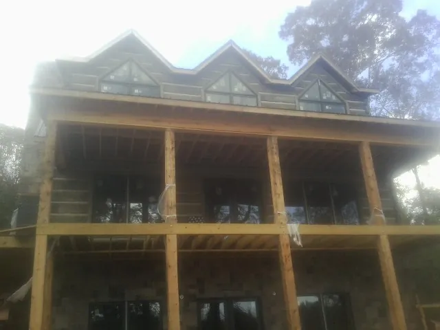 Dormers and porch framing on a large log home under construction — Roof Coating work by our crew in Milano