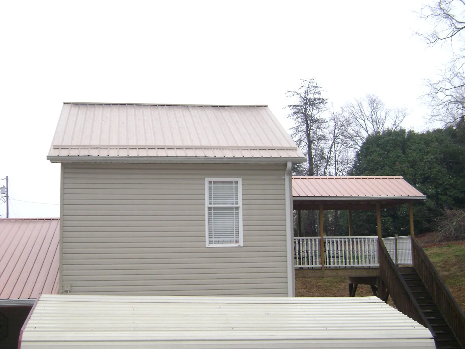 Tan metal roofs on a two story addition and attached porch, from a Roof Replacement job in Milano
